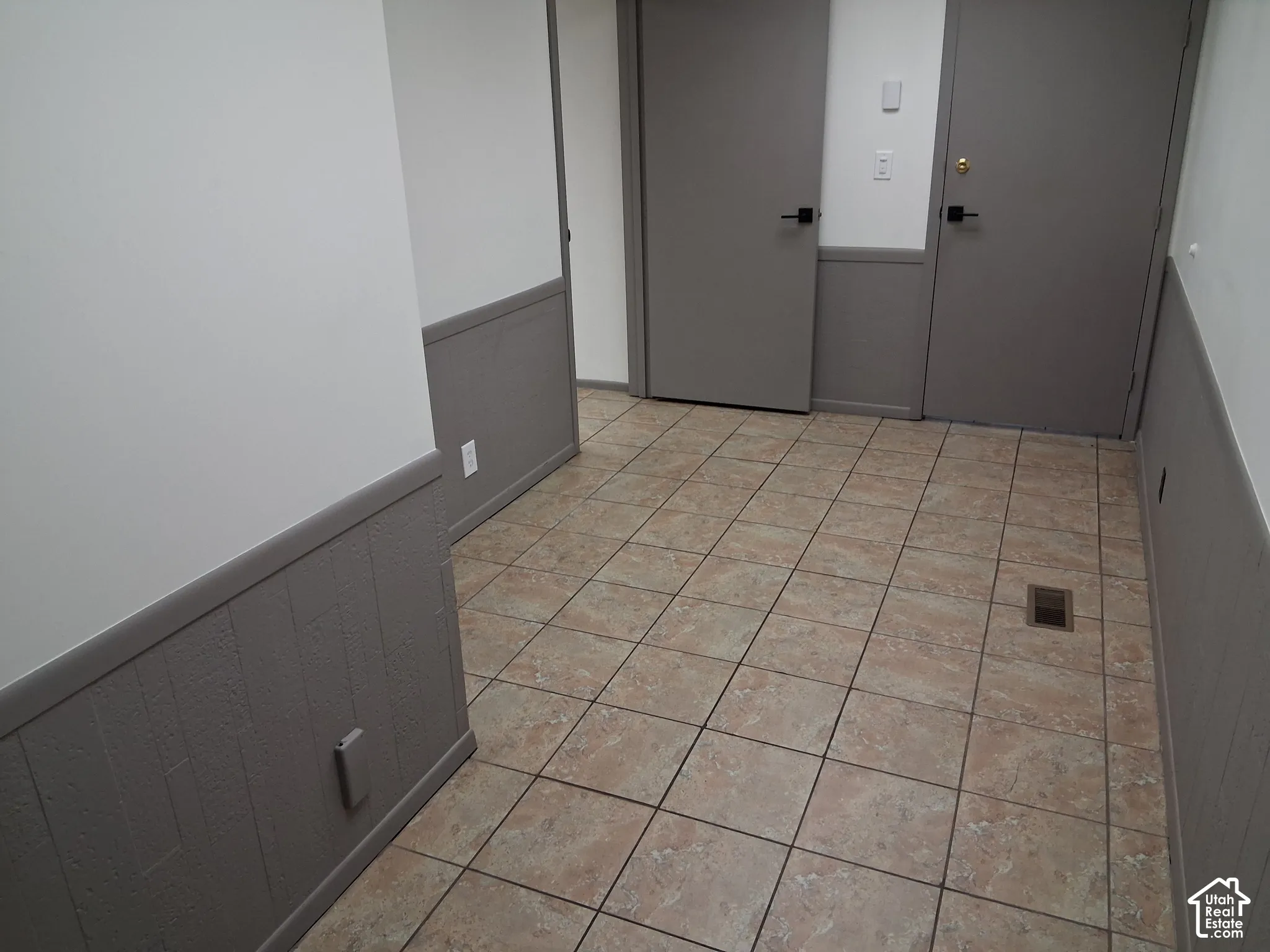 Ceramic tile flooring featuring neutral tones with gray wainscoting, solid-core interior doors, and matte black hardware