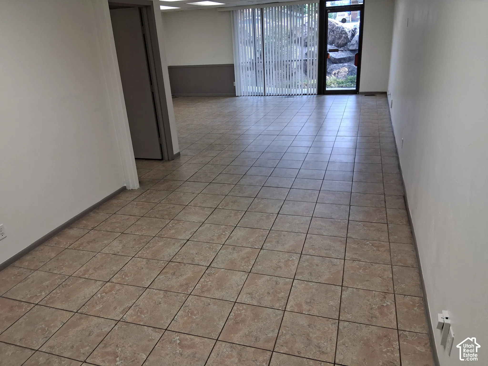 Open floor plan featuring tile flooring, neutral wall tones, recessed lighting, and vertical window blinds leading to a glass-paneled entry door