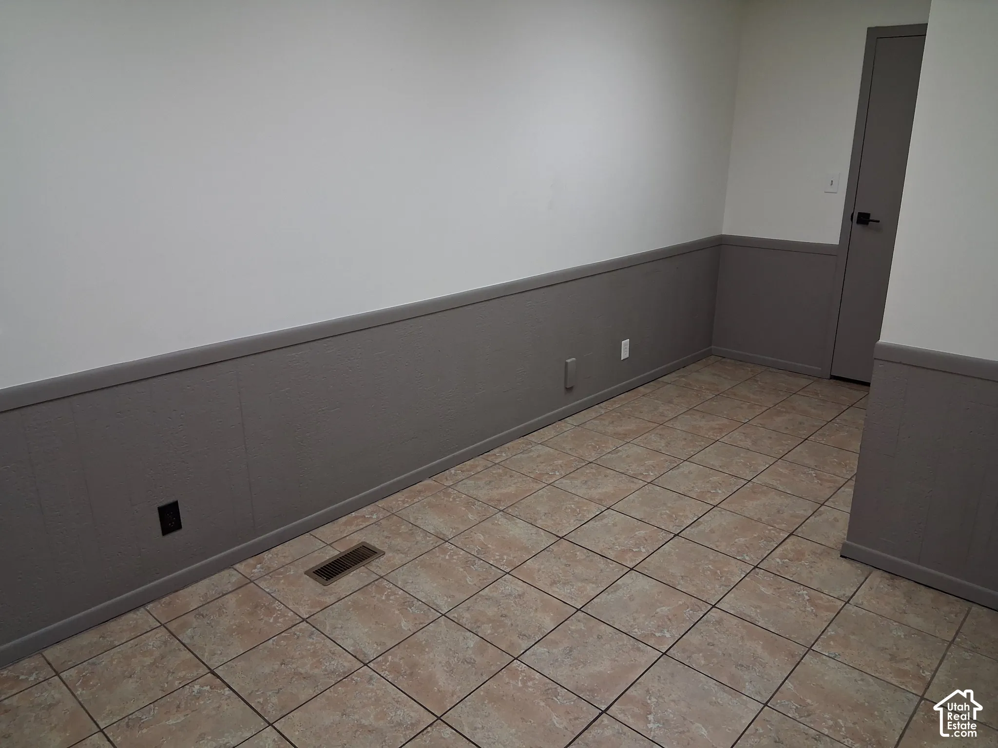 Interior room featuring neutral-toned tile flooring, gray wainscoting with a chair rail, and a solid-panel door with matte black hardware