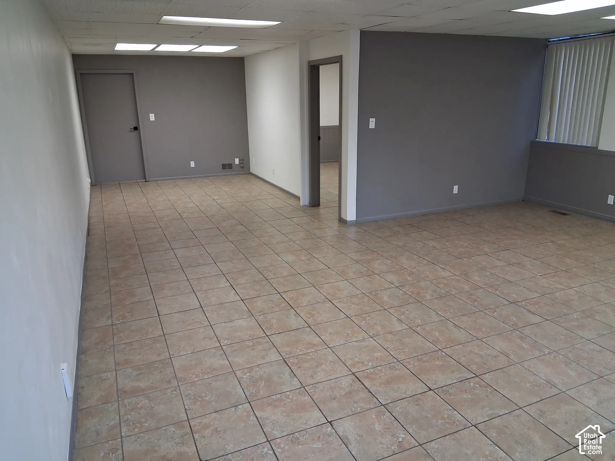 Open-concept room featuring neutral-toned ceramic tile flooring, recessed grid ceiling lighting, and vertical window blinds