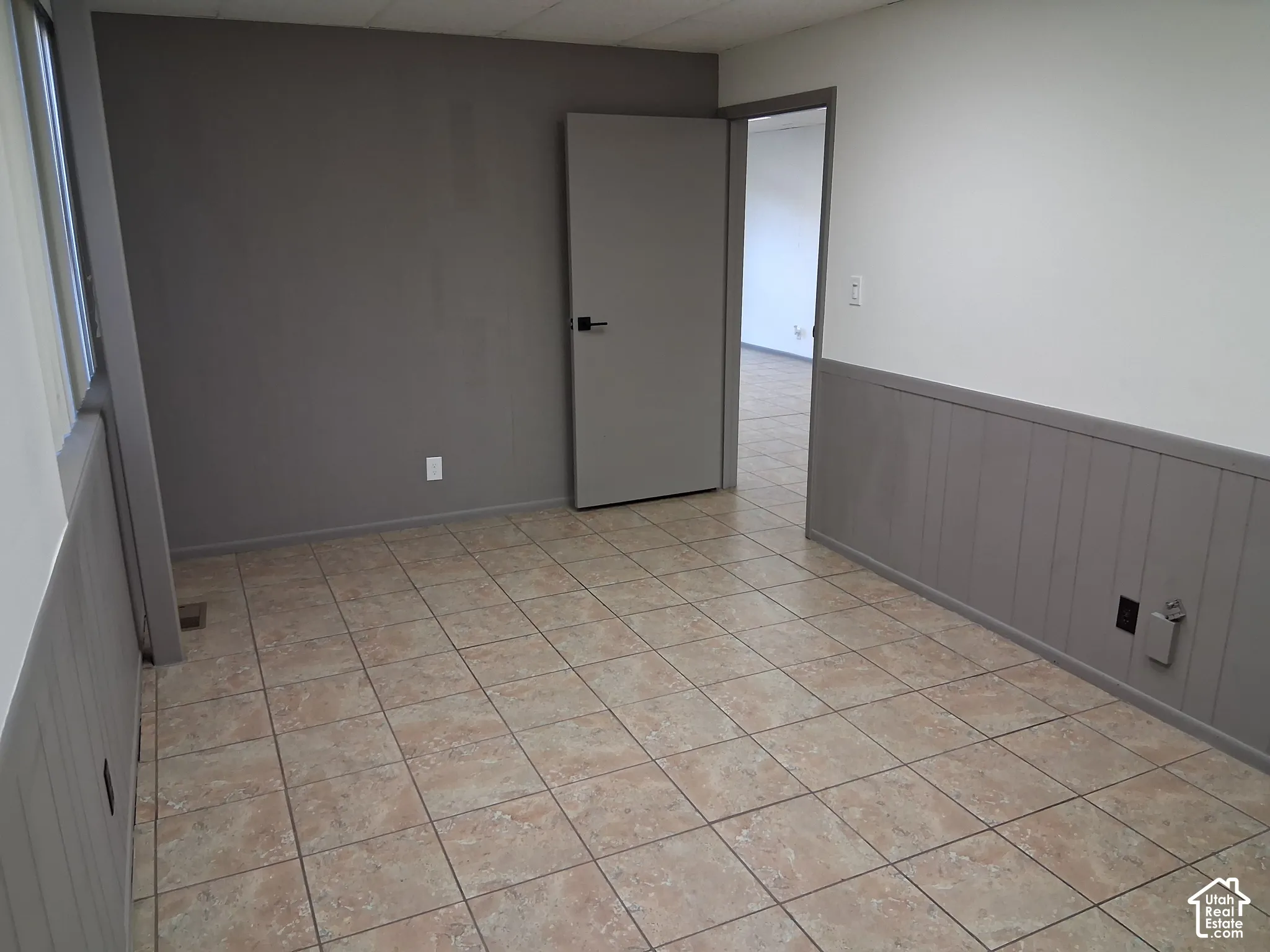 Interior space featuring ceramic tile flooring, neutral wall-to-wall wainscoting, and a flat-panel door with matte black hardware