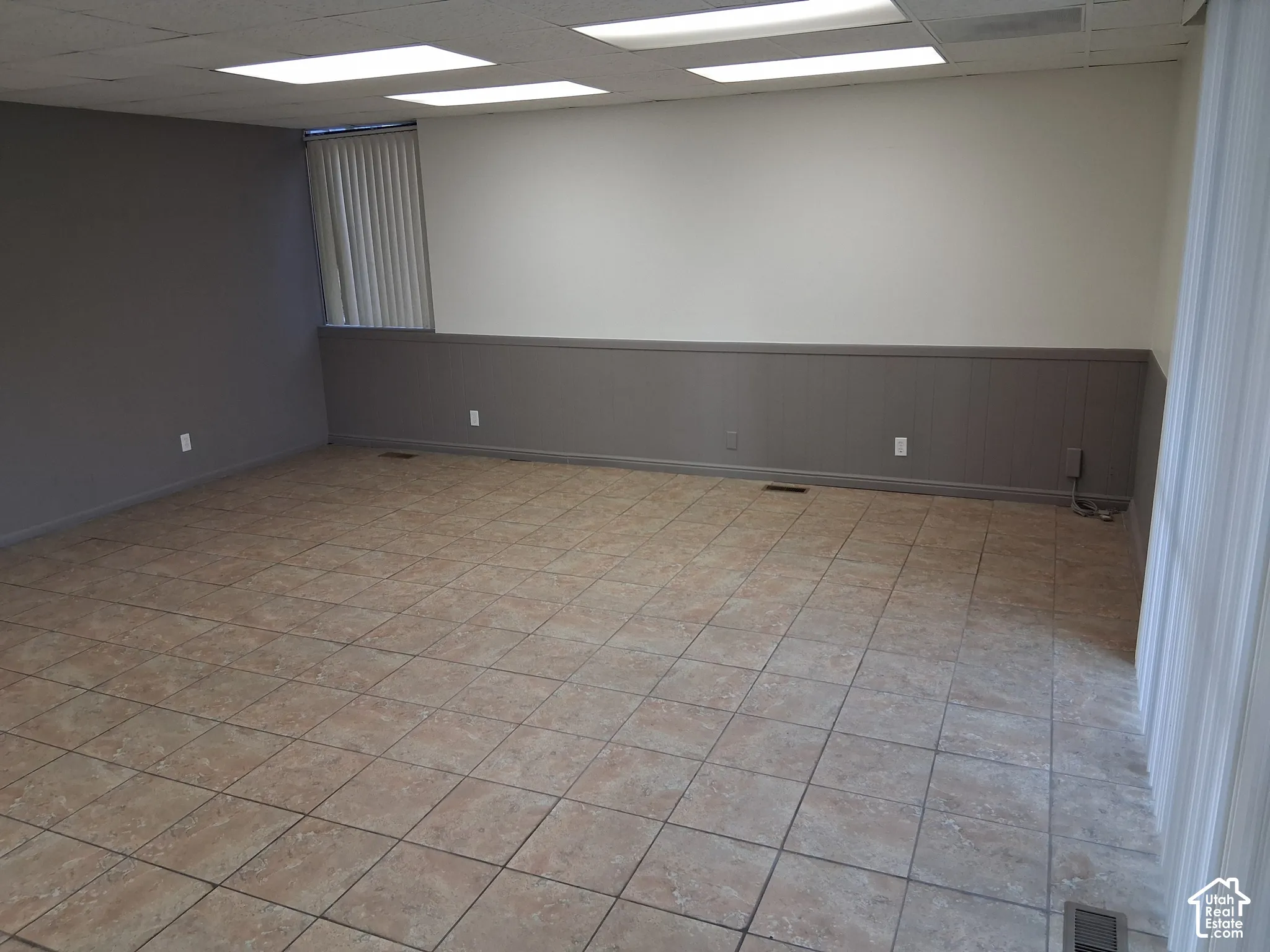 Spacious room featuring tile flooring, wainscoting, recessed lighting, and vertical window blinds