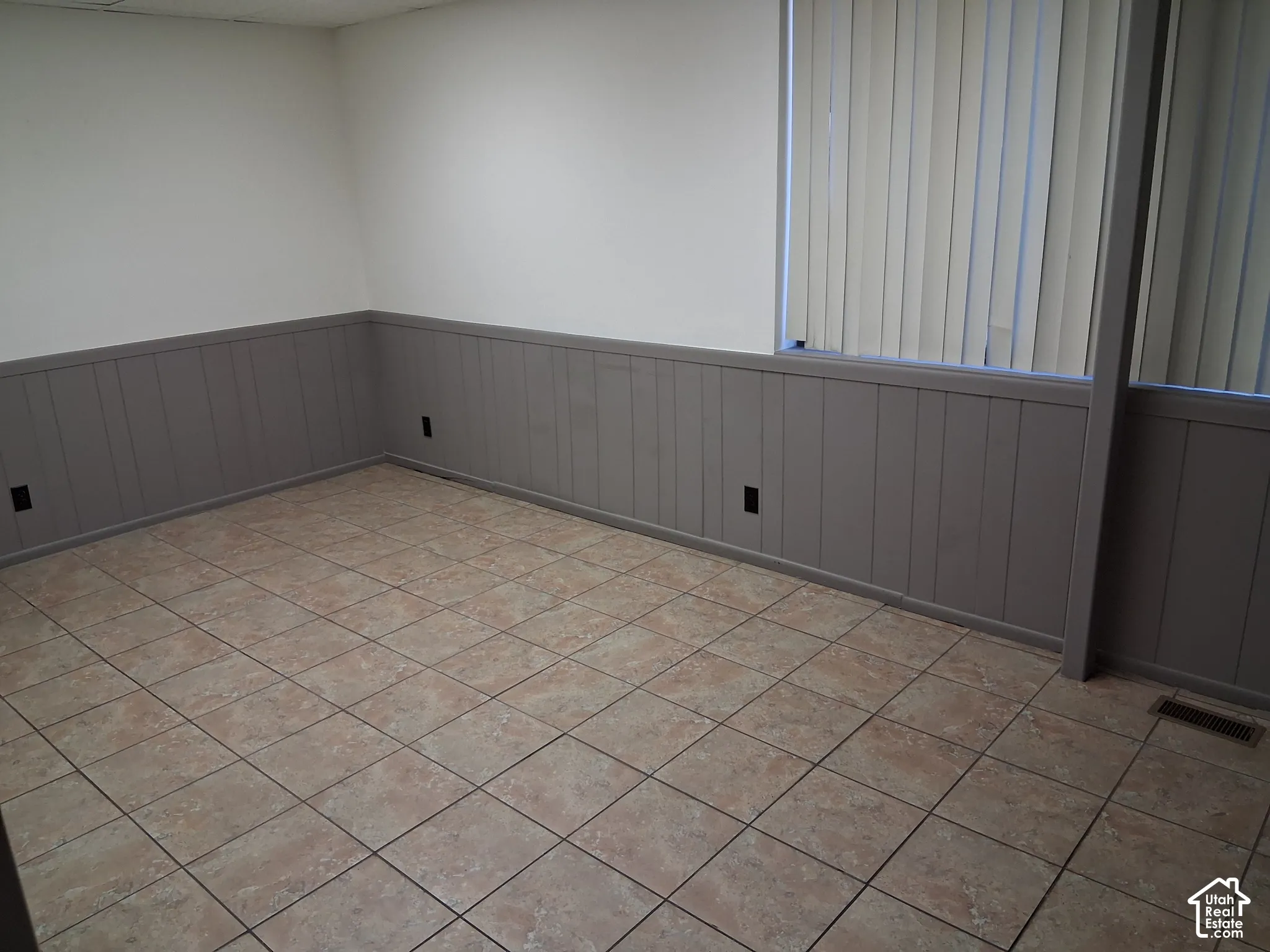 Interior room featuring neutral-toned tile flooring, gray wainscoting, and vertical blinds