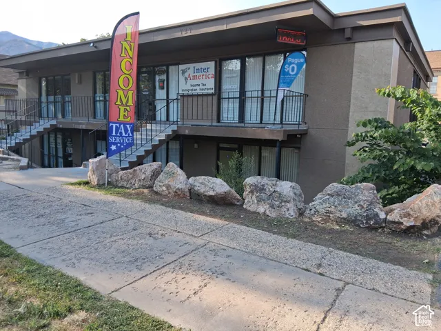 Two-story commercial exterior featuring concrete construction, metal staircases, full-length glass storefronts, and boulder landscape accents
