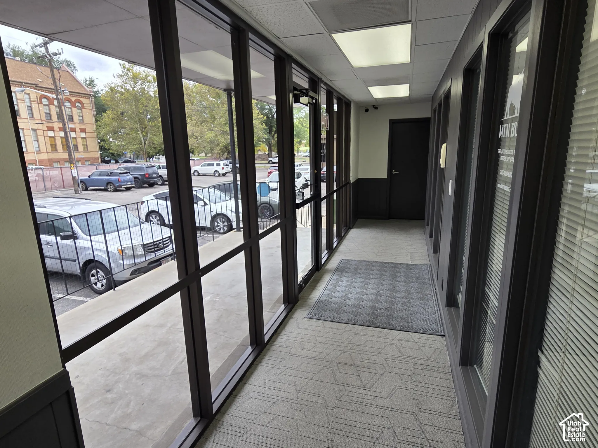 Interior hallway featuring floor-to-ceiling dark-framed glass wall panels, recessed lighting, and patterned carpeted flooring