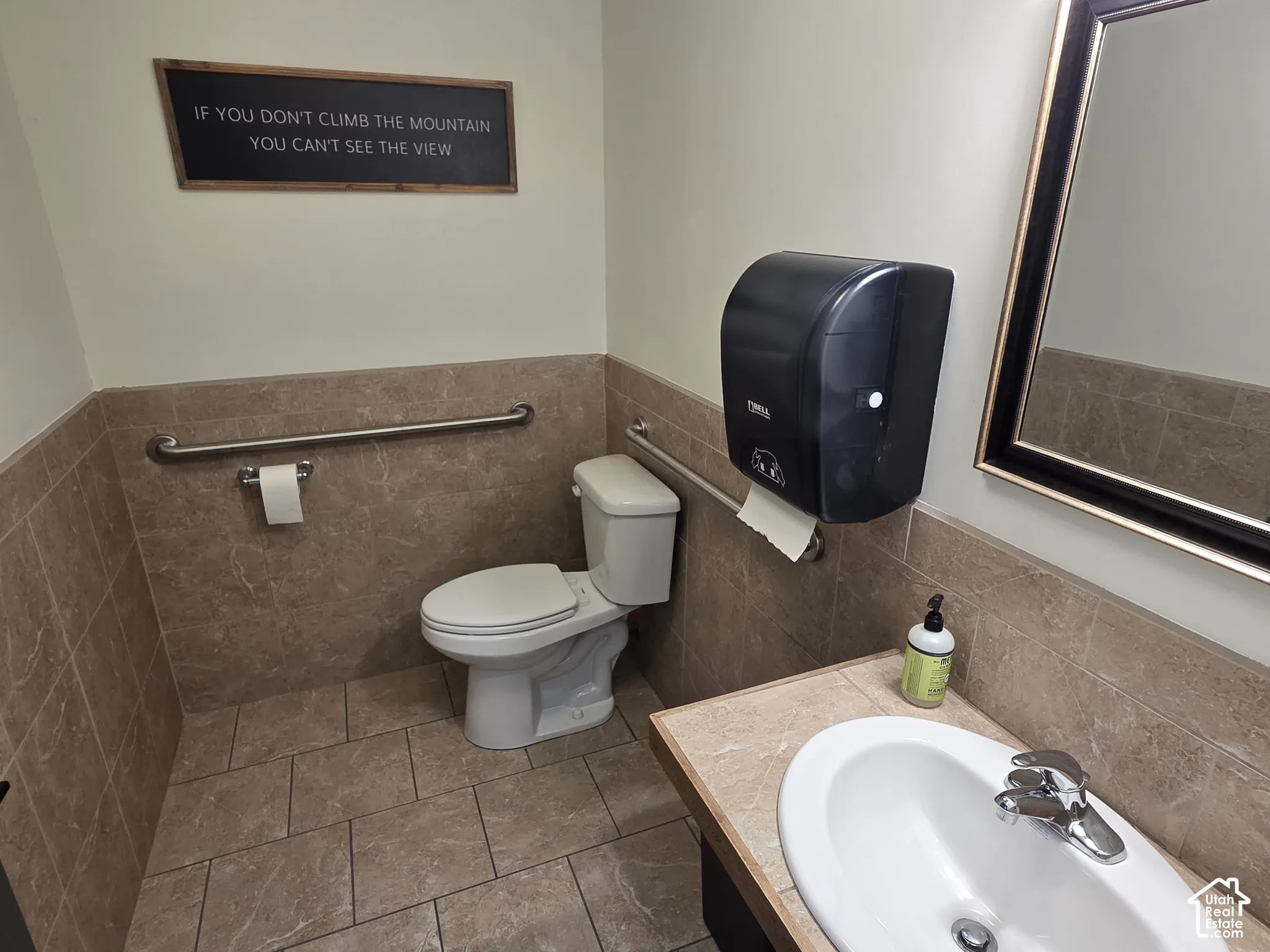 Restroom featuring ceramic tile flooring and wall wainscoting, a pedestal sink with a chrome faucet, and horizontal metal grab bars