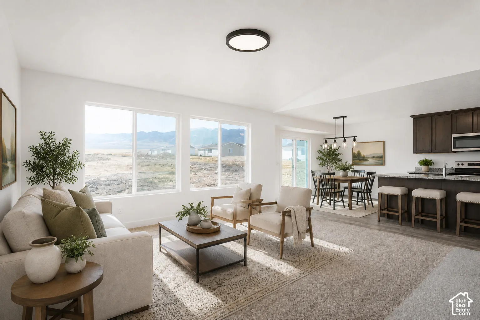 Open-concept interior featuring high vaulted ceilings, large picture windows with mountain backdrop, dark-toned cabinetry, kitchen island with stone-surface countertop, and flush-mount lighting