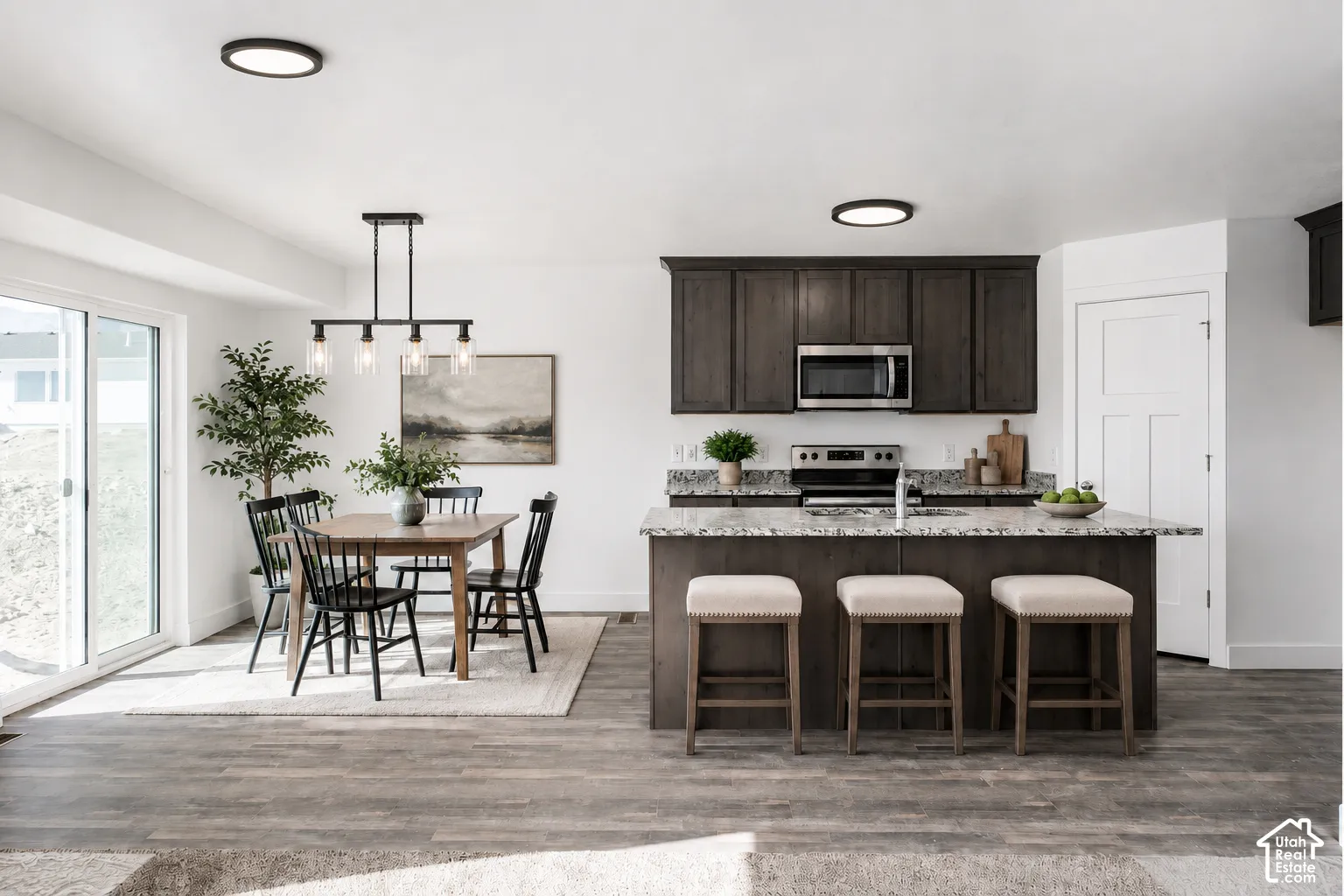 Kitchen featuring dark-finish cabinetry, an island with stone-style countertops, wood-finish flooring, and a linear four-light pendant fixture