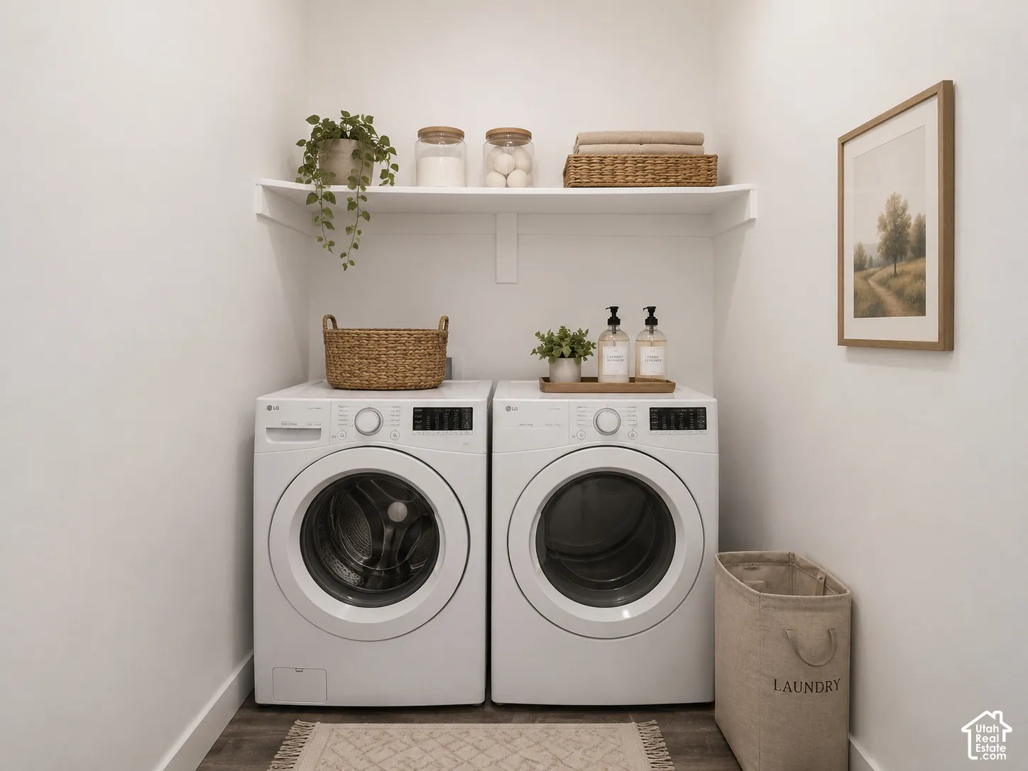 Laundry area featuring white front-load appliances and a fixed overhead white shelf with wood-finish flooring