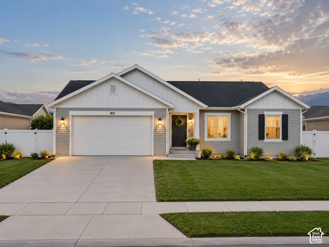 Single-level exterior featuring light-gray horizontal siding, white vertical board-and-batten accents, a concrete driveway, attached two-car garage, and white vinyl privacy fencing