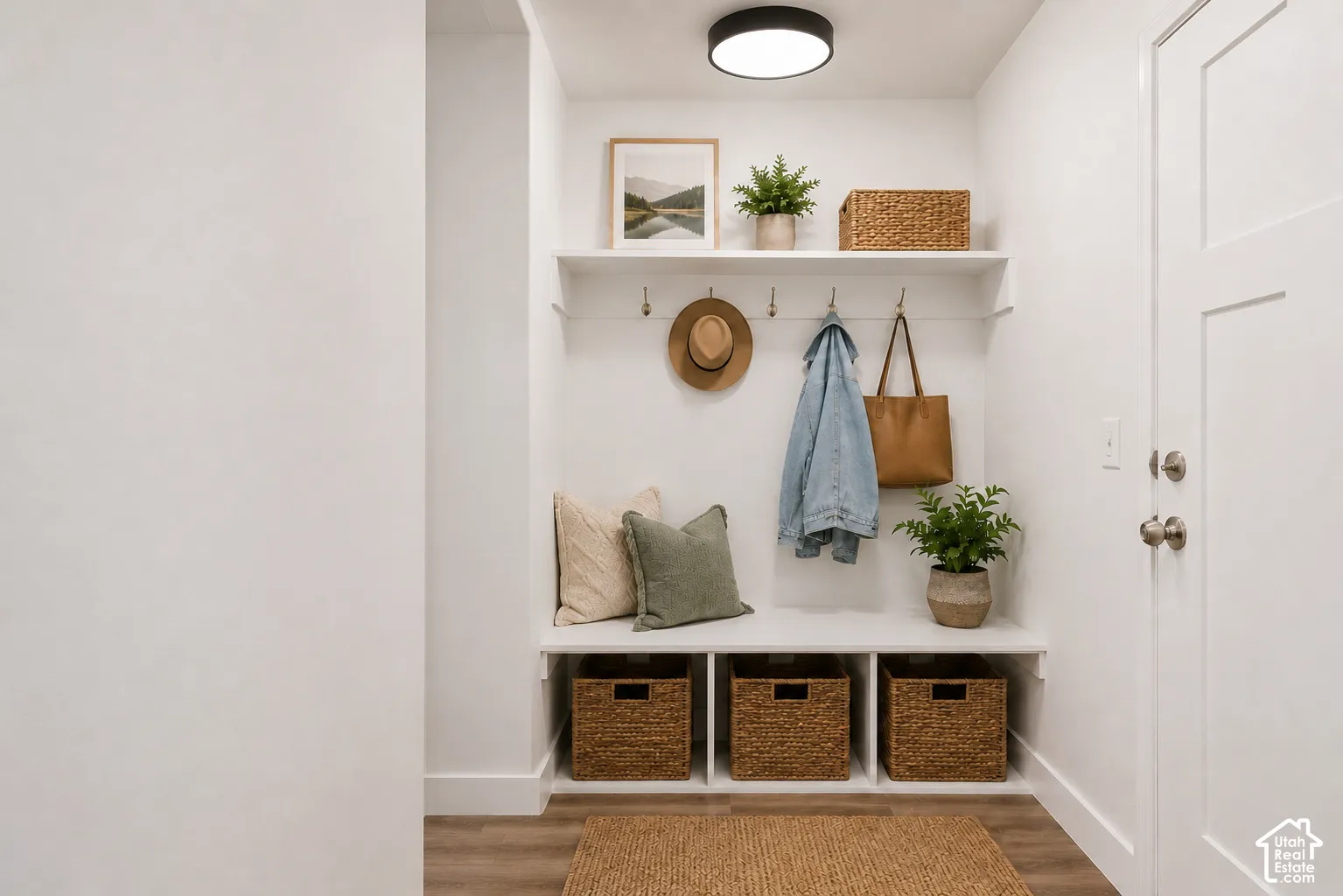 Built-in mudroom nook featuring a bench with three-compartment storage, overhead shelving, metallic wall hooks, and a circular ceiling-mounted flush light fixture
