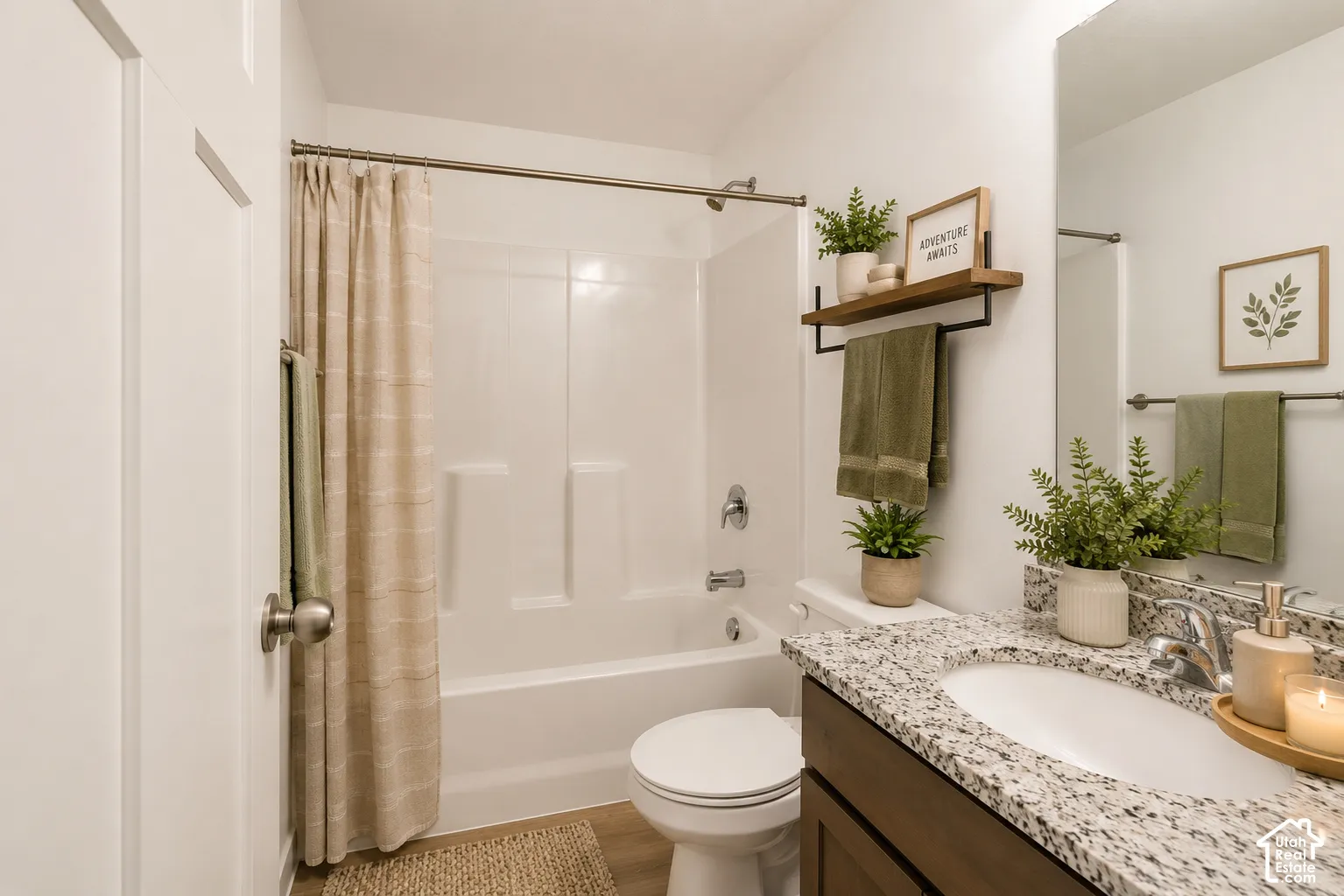 Bathroom featuring a vanity with speckled composite countertop, integrated oval sink, and dark-toned cabinetry, paired with a white acrylic tub-shower surround and wood-finish flooring