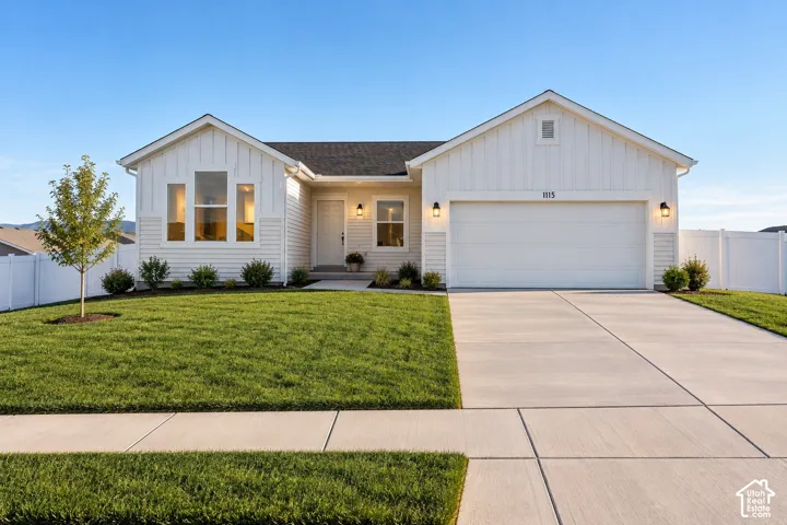 Single-story exterior featuring white board-and-batten siding, a dual-gabled roofline, an attached two-car garage, and white vinyl privacy fencing