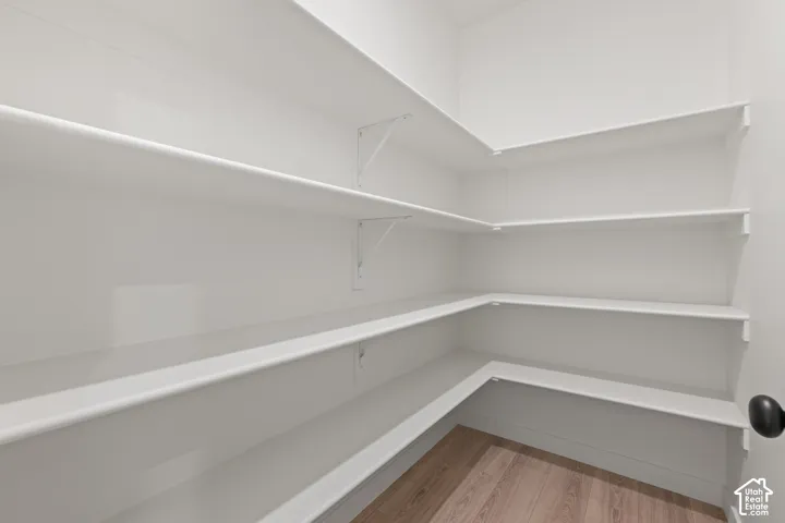 Storage area featuring multi-level wrap-around shelving with white-finished surfaces, mounted on white brackets, complemented by wood-finish flooring