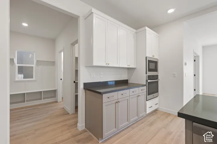 Kitchen area featuring dual-tone cabinetry, solid surface countertops, a built-in wall oven and microwave combination, recessed lighting, and wood-finish flooring