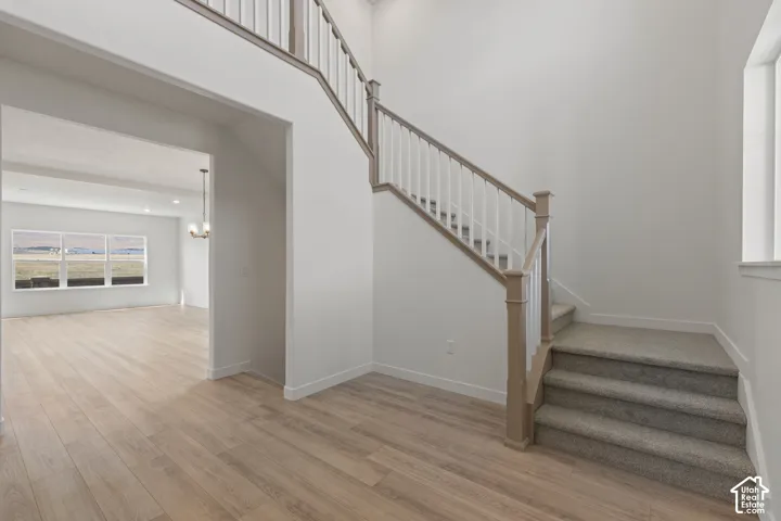 Two-story foyer featuring wood-finish flooring, a staircase with a wooden handrail and white balusters, and neutral-toned wall-to-wall carpeting