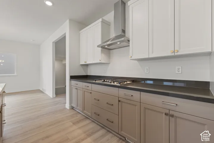 Kitchen featuring dual-tone cabinetry, dark solid-surface countertops, a stainless steel gas cooktop, and an integrated stainless steel range hood