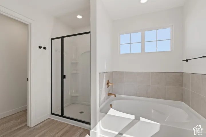 Standalone shower with black-frame enclosure, deep soaking tub, neutral tile surround, and wood-finish flooring