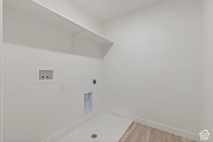 Utility space featuring wood-finish flooring, a white overhead shelf, recessed laundry hookups, and a floor drain