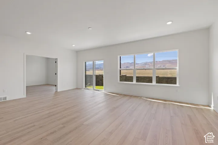 Open-concept interior featuring light wood-finish flooring, recessed lighting, large picture windows, sliding glass door, and mountain backdrop