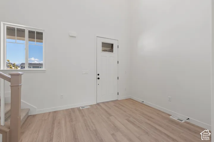 High-ceiling interior featuring wood-finish flooring, a white-paneled exterior door with a glass inset, and a double-hung window
