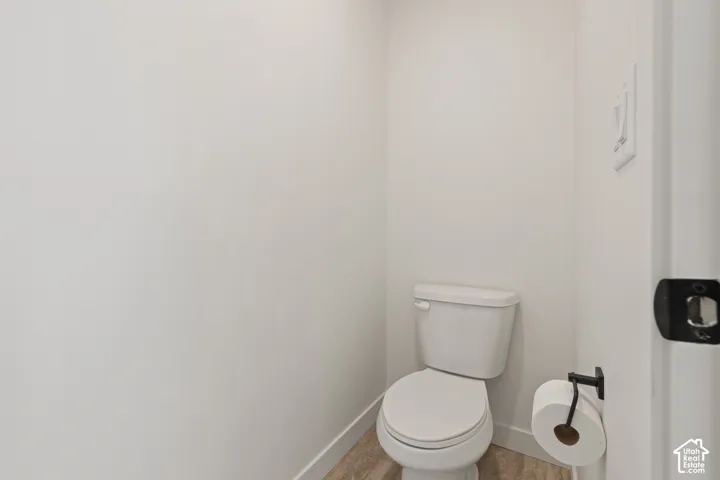 Neutral-toned interior featuring a white porcelain commode, matte black toilet paper holder, and wood-finish flooring