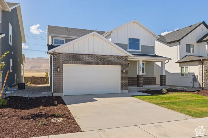 Two-story exterior featuring a brick and vertical siding facade, covered front porch with square columns, two-car garage, and desert mountain backdrop