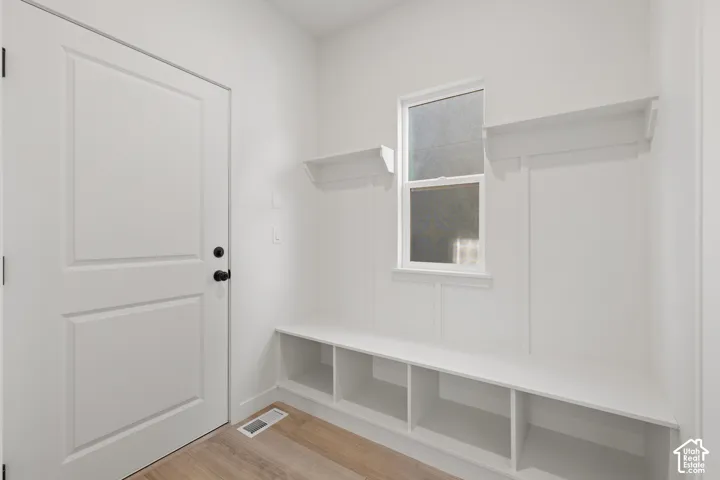 Built-in mudroom bench featuring partitioned storage cubbies, integrated wall shelving, vertical board-and-batten millwork, and wood-finish flooring
