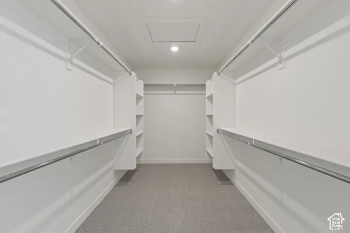 Walk-in closet featuring white built-in shelving, dual-tier metal hanging rods, and neutral carpeting