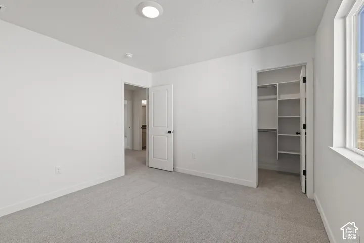 Interior room featuring neutral wall-to-wall carpeting, crisp white walls, a walk-in closet with built-in shelving, and a dual-pane window