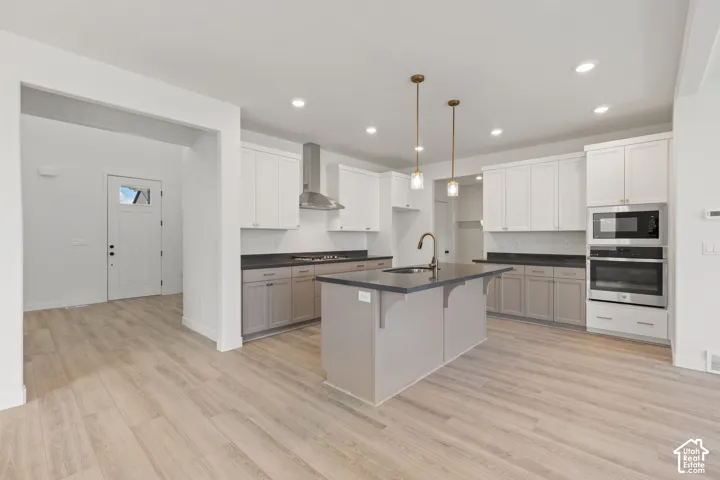 Kitchen featuring dual-tone cabinetry, dark countertops, a central island with an integrated sink, stainless steel appliances, and recessed lighting