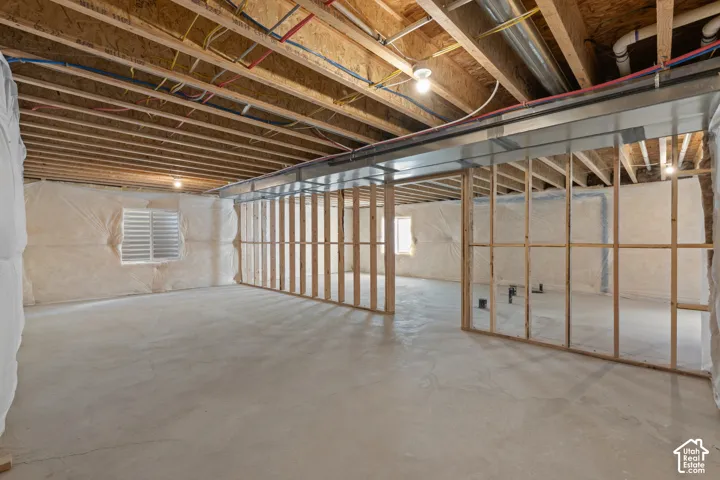Unfinished basement featuring exposed wood joists, concrete flooring, insulated wall barriers, and metal ductwork