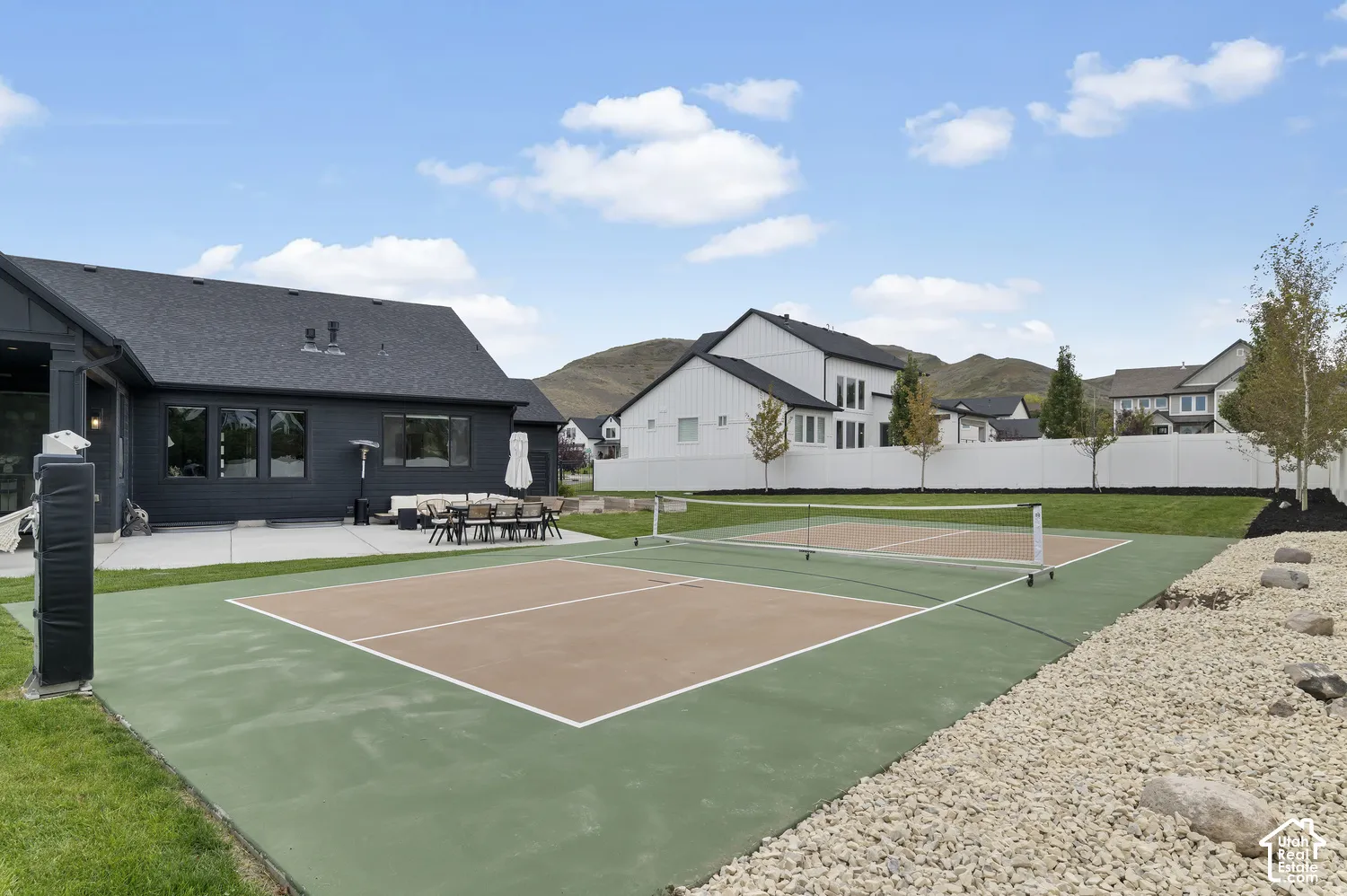 Backyard featuring a dedicated pickleball court, concrete patio, manicured lawn, white vinyl fencing, and mountain backdrop