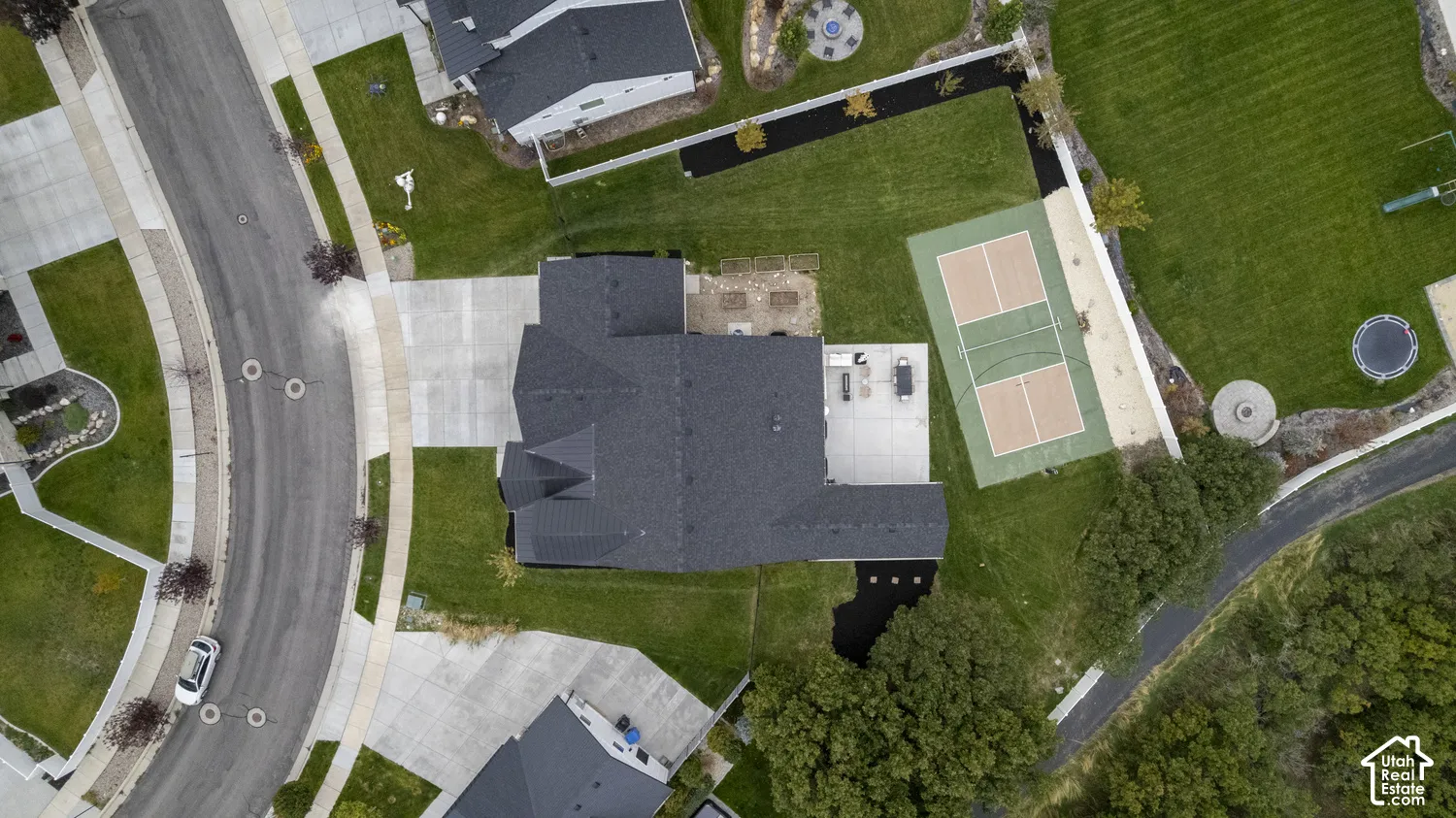 Aerial view of residential property featuring a dedicated pickleball court, concrete patio, multi-car driveway, and landscaped yard