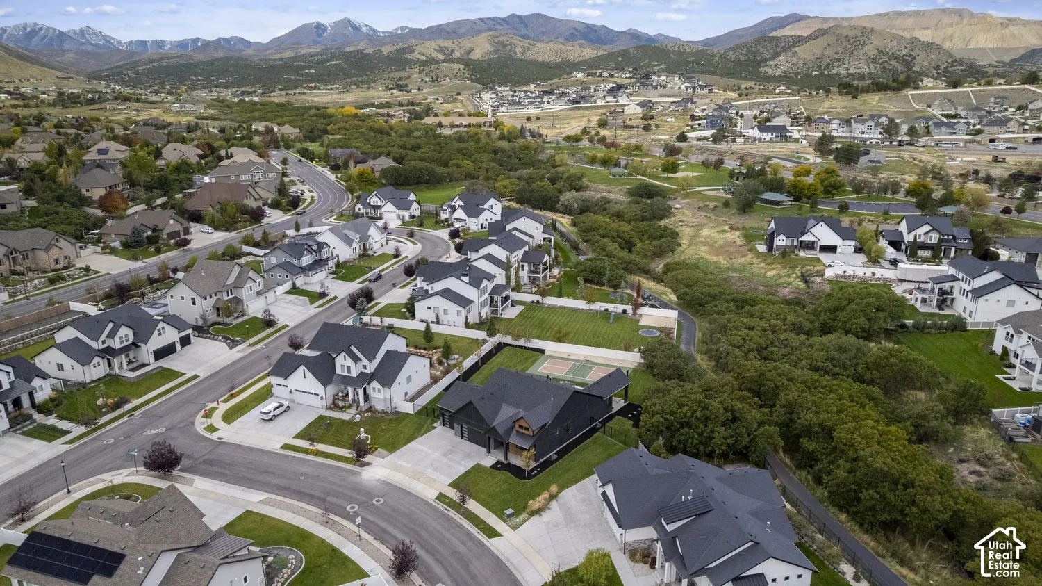 Aerial perspective of residential property featuring a multi-car garage, private sport court, manicured lawn, and mountain backdrop
