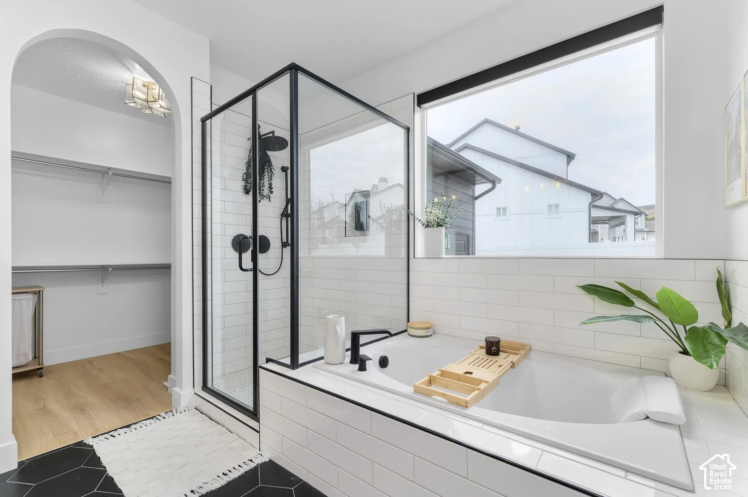 Soaking tub and separate glass-enclosed shower with matte black fixtures, white subway tile surround, arched entryway, and hexagonal floor tile