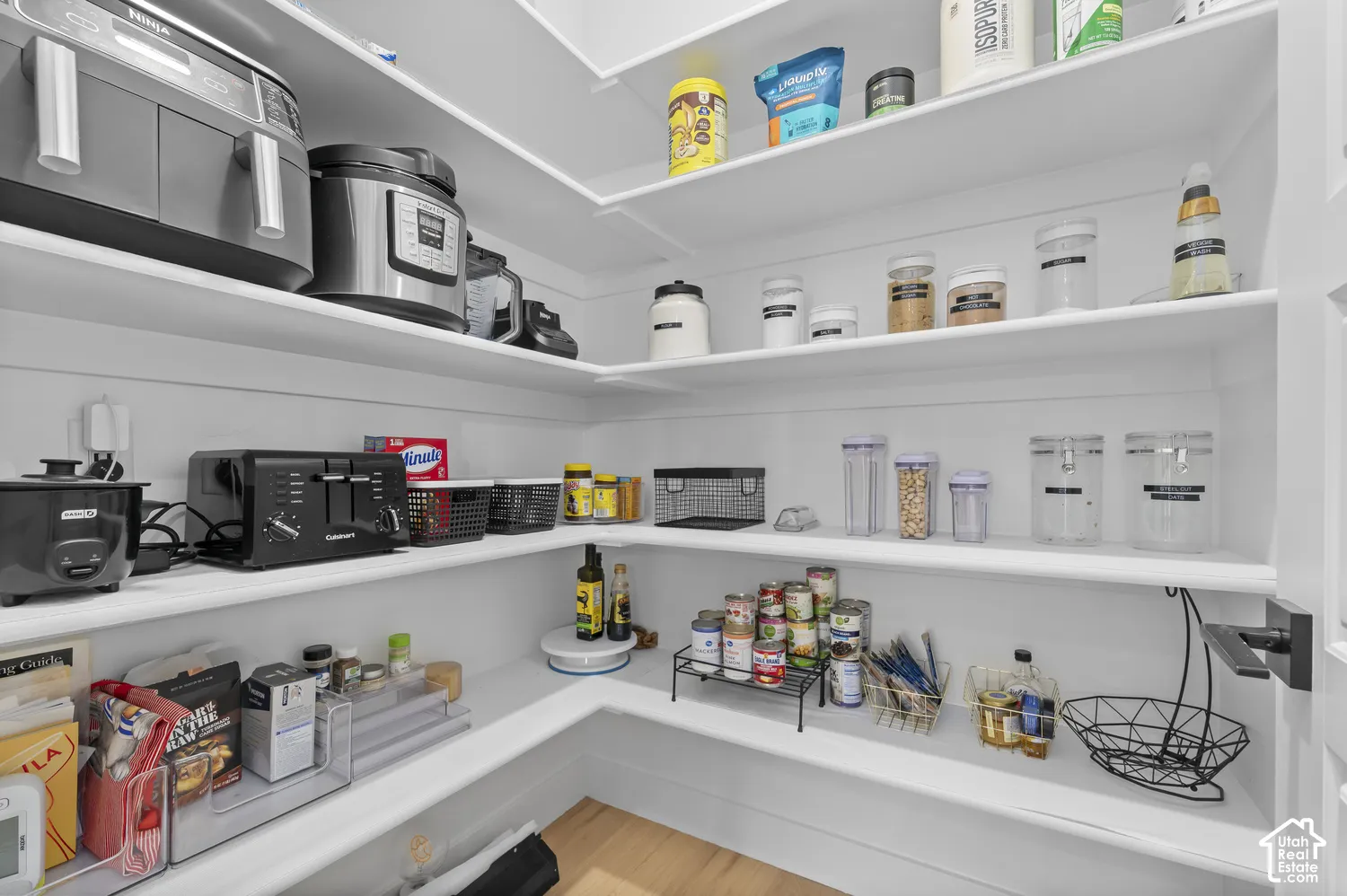 Walk-in pantry featuring white wrap-around shelving, wood-finish flooring, and a matte black door handle