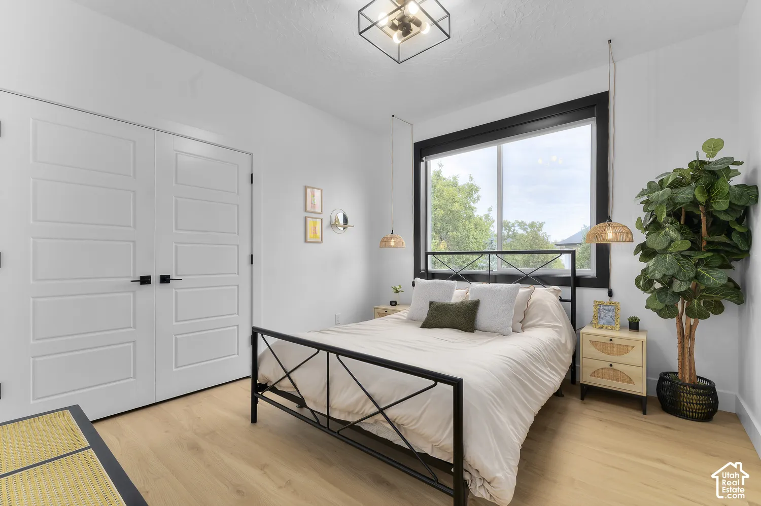 Neutral interior featuring wood-finish flooring, white double doors with matte black hardware, a window with a bold black frame, a geometric flush-mount light fixture, and dual woven-style pendant lights