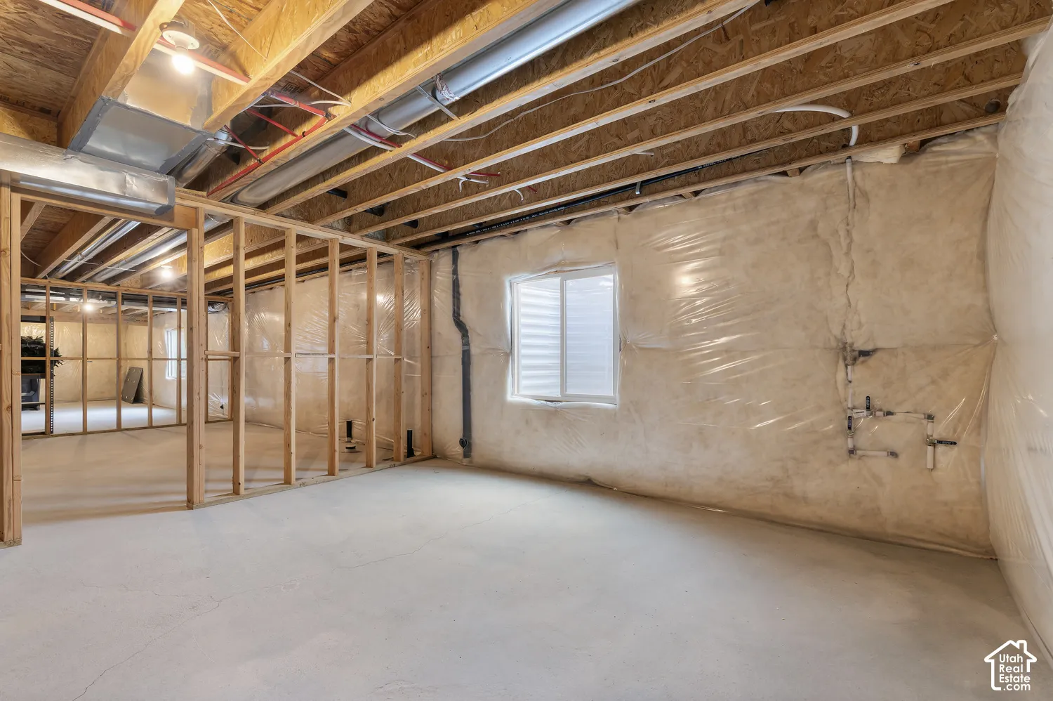 Unfinished lower level featuring exposed wood framing, concrete flooring, exterior-grade window, and vapor-barrier insulation