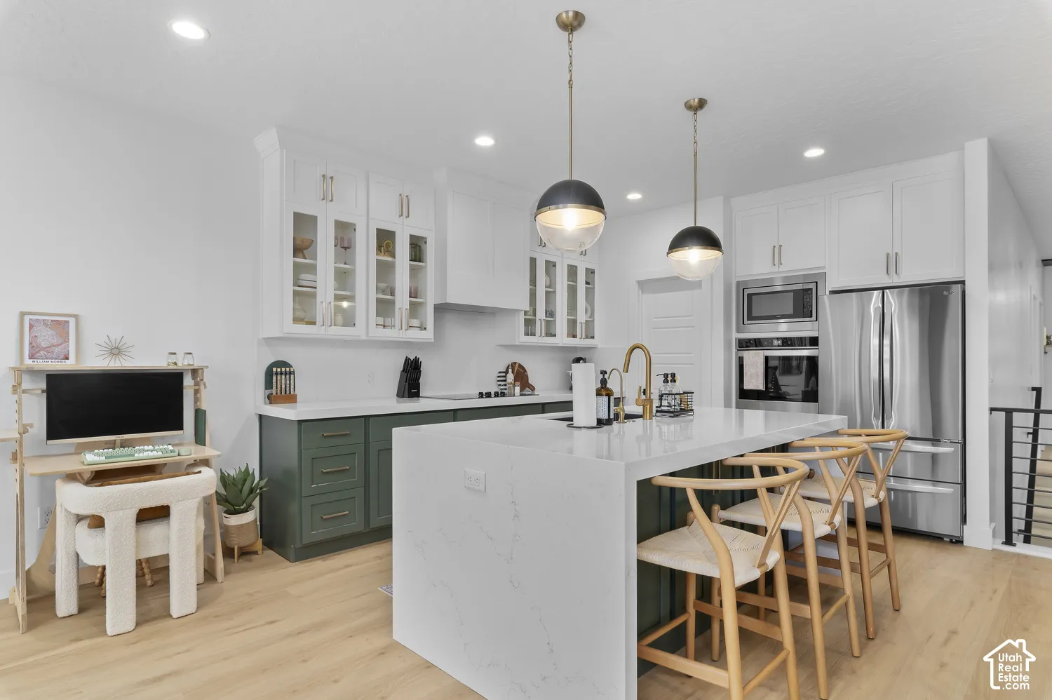 Kitchen featuring a central island with waterfall-edge countertop, two-toned shaker-style cabinetry, recessed ceiling lighting, glass-front upper cabinets, and integrated stainless steel appliances