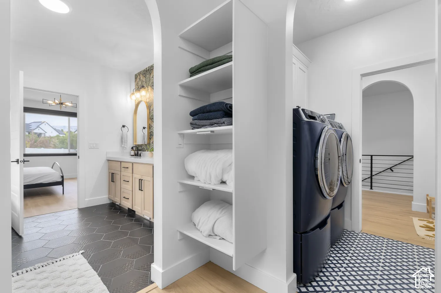 Built-in shelving with multiple storage tiers, vanity featuring a light-toned wood finish and stone countertop, geometric tile flooring, and arched architectural doorways