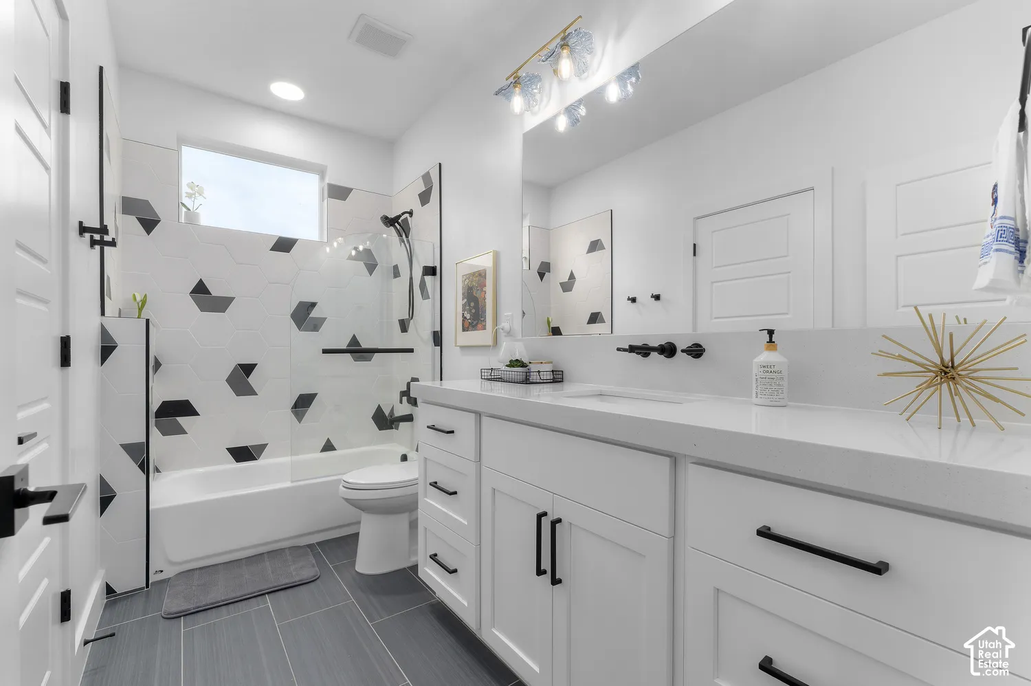 Bathroom featuring a white vanity with quartz countertop, wall-mounted matte black faucet, full-width mirror, and shower surround with geometric tile accents