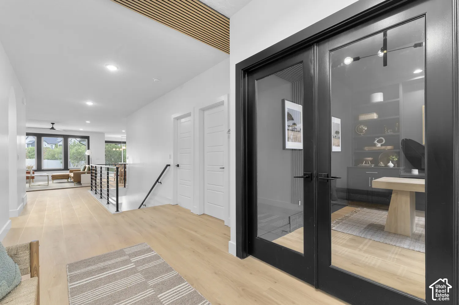 Interior space featuring light wood-finish flooring, black-framed glass French doors, linear slat ceiling detailing, and a black metal stair railing