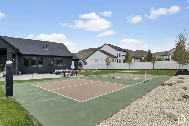 Backyard featuring a dedicated pickleball court, concrete patio, manicured lawn, white vinyl fencing, and mountain backdrop