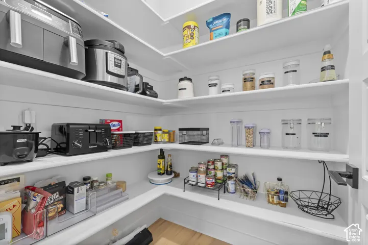 Walk-in pantry featuring white wrap-around shelving, wood-finish flooring, and a matte black door handle