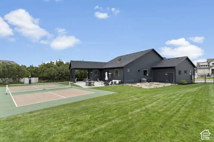 Expansive backyard featuring a pickleball court, covered concrete patio, stone-bordered fire pit, and manicured lawn