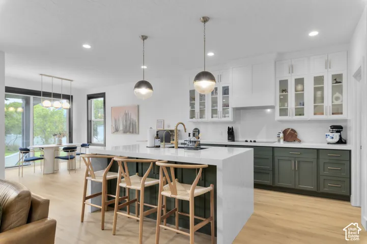 Kitchen featuring a waterfall-edge island, two-tone cabinetry, glass-front upper cabinets, quartz countertops, and wood-finish flooring