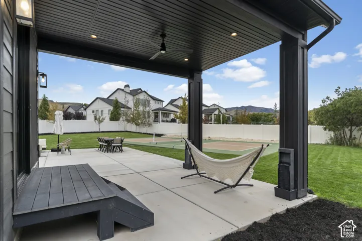 Covered concrete patio featuring a black-finished tongue-and-groove ceiling with recessed lighting and a ceiling fan, a tiered wood-finish staircase, and a dedicated sport court