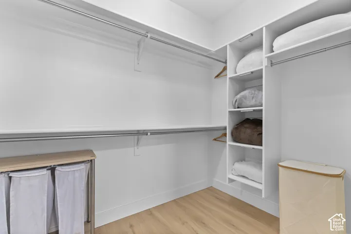 Walk-in closet featuring white built-in shelving, tiered metal hanging rods, and wood-finish flooring