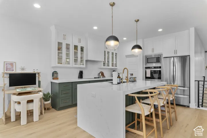 Kitchen featuring a central island with waterfall-edge countertop, two-toned shaker-style cabinetry, recessed ceiling lighting, glass-front upper cabinets, and integrated stainless steel appliances